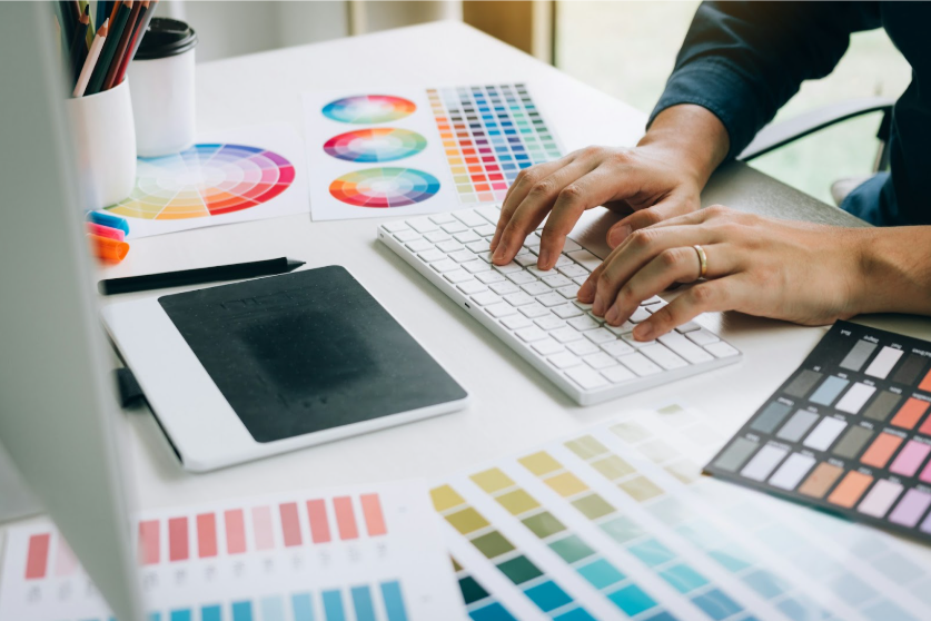 A designer sits at a computer with color palettes around them